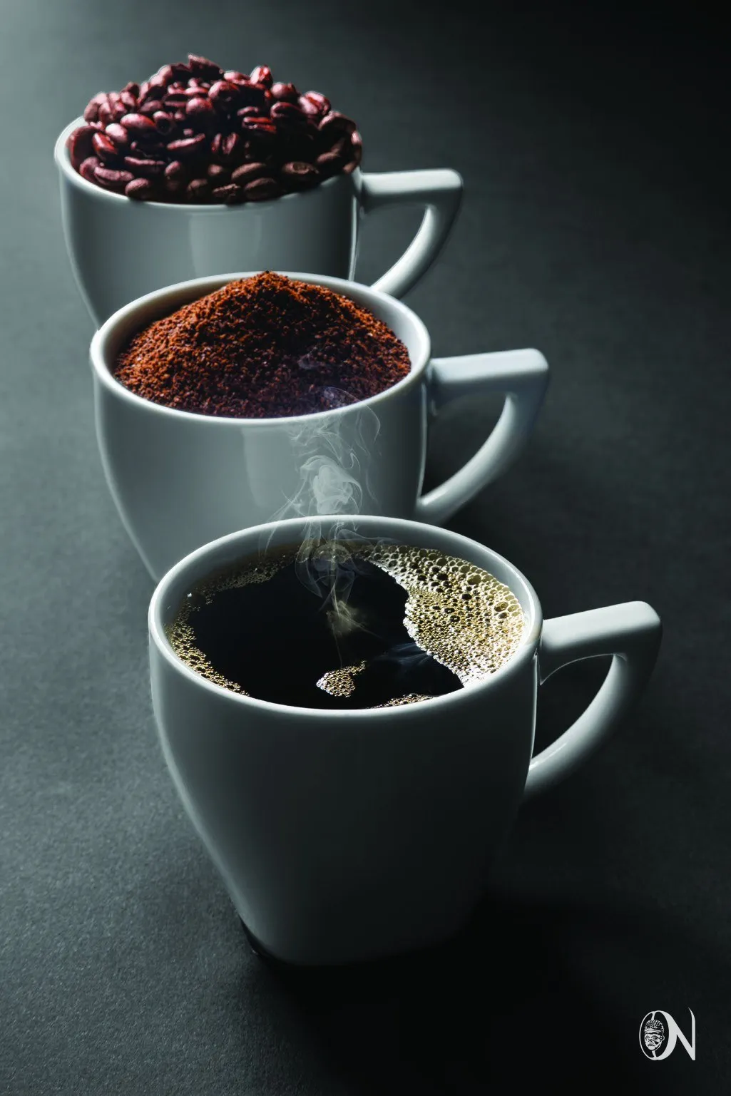 Three ceramic cups holding whole beans, grounds and brewed coffee
